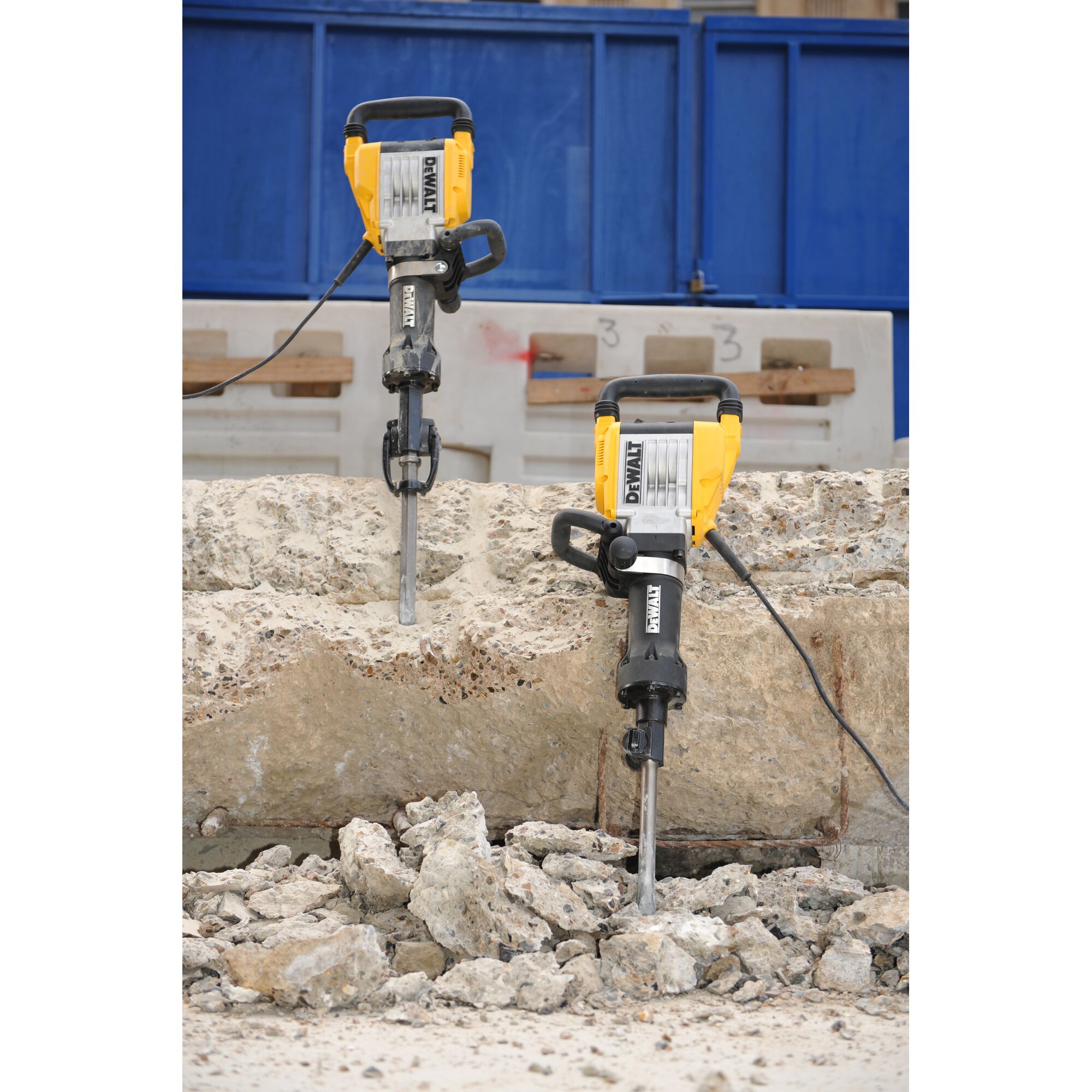 Two DEWALT electric demolition jackhammers are shown breaking up a large concrete slab at a construction site, with rubble scattered on the ground.