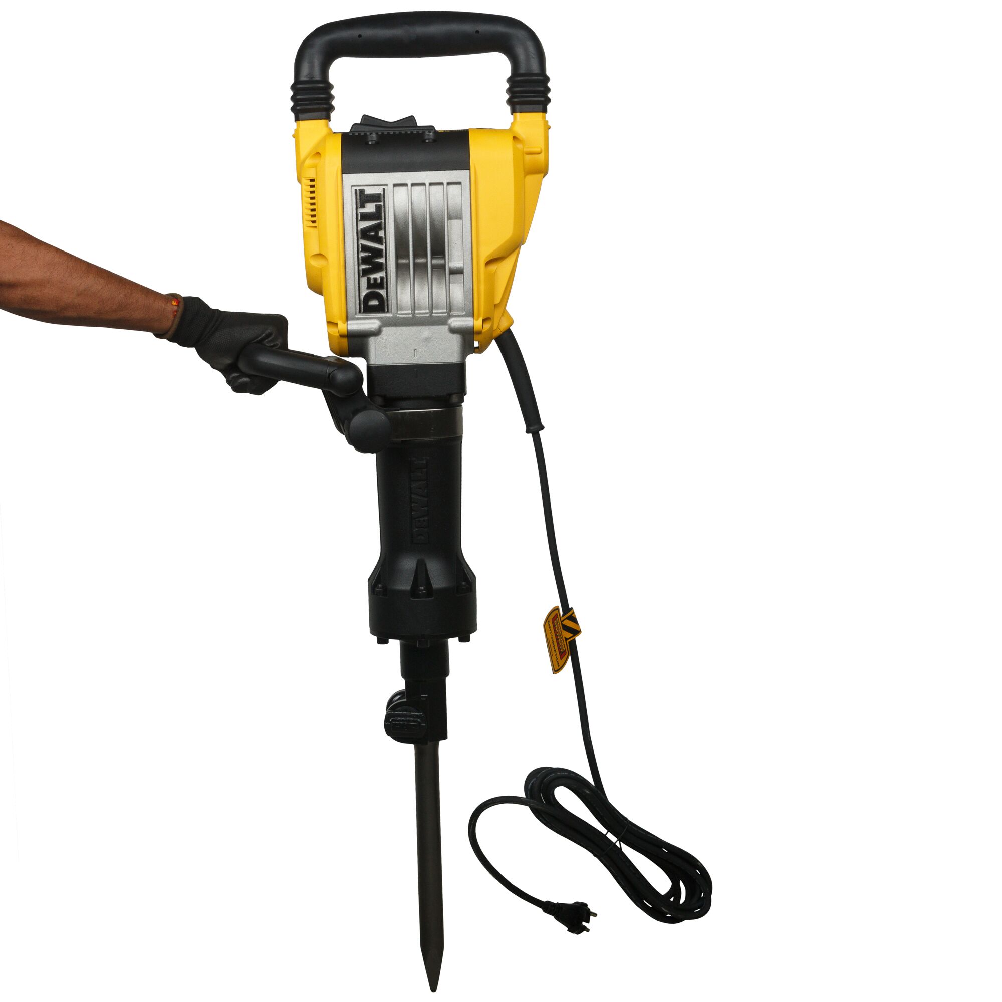 A person wearing a glove is holding a DEWALT electric demolition hammer with a pointed chisel bit and a long power cord attached.