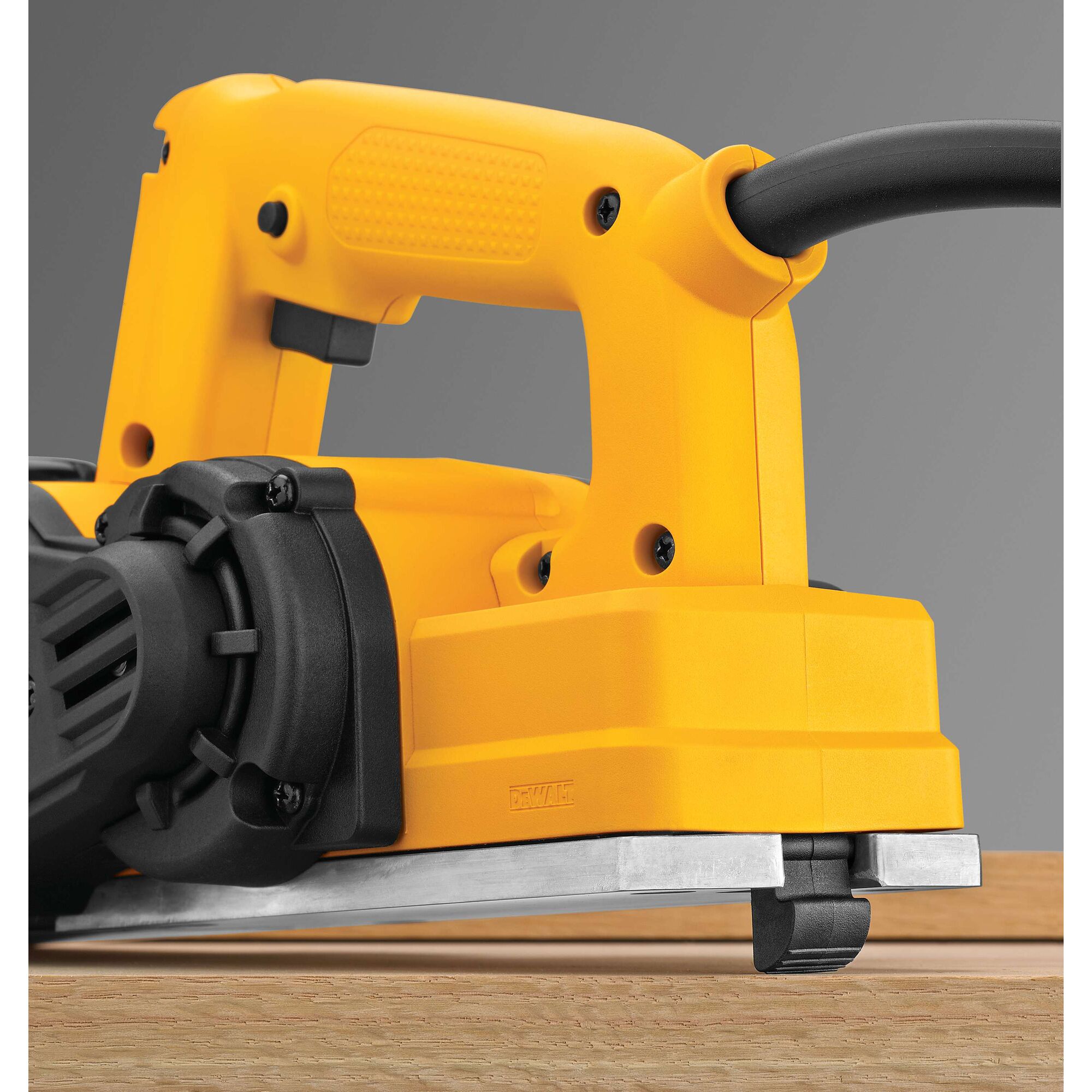 Close-up view of a yellow DEWALT electric hand planer being used on a wooden surface, showing the handle, power cord, and part of the base plate.