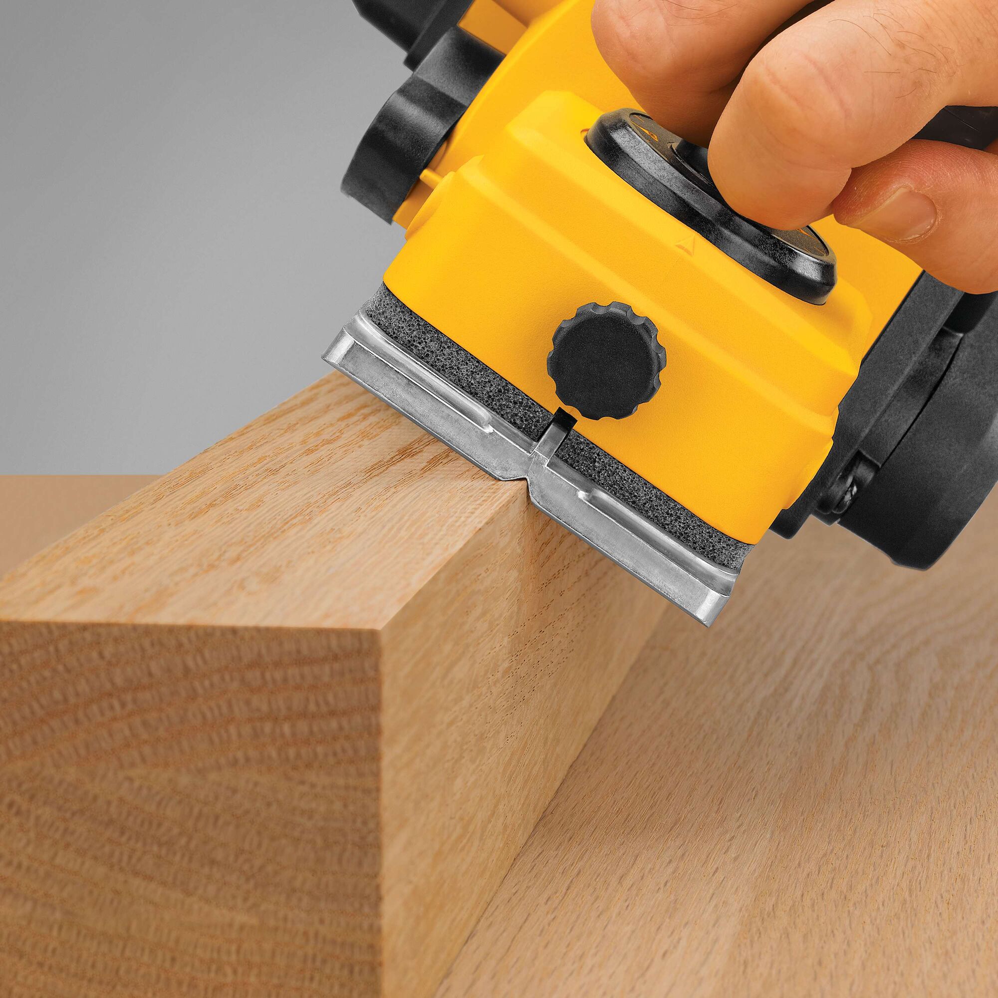 Close-up of a yellow DEWALT electric planer being used to smooth the edge of a wooden plank.