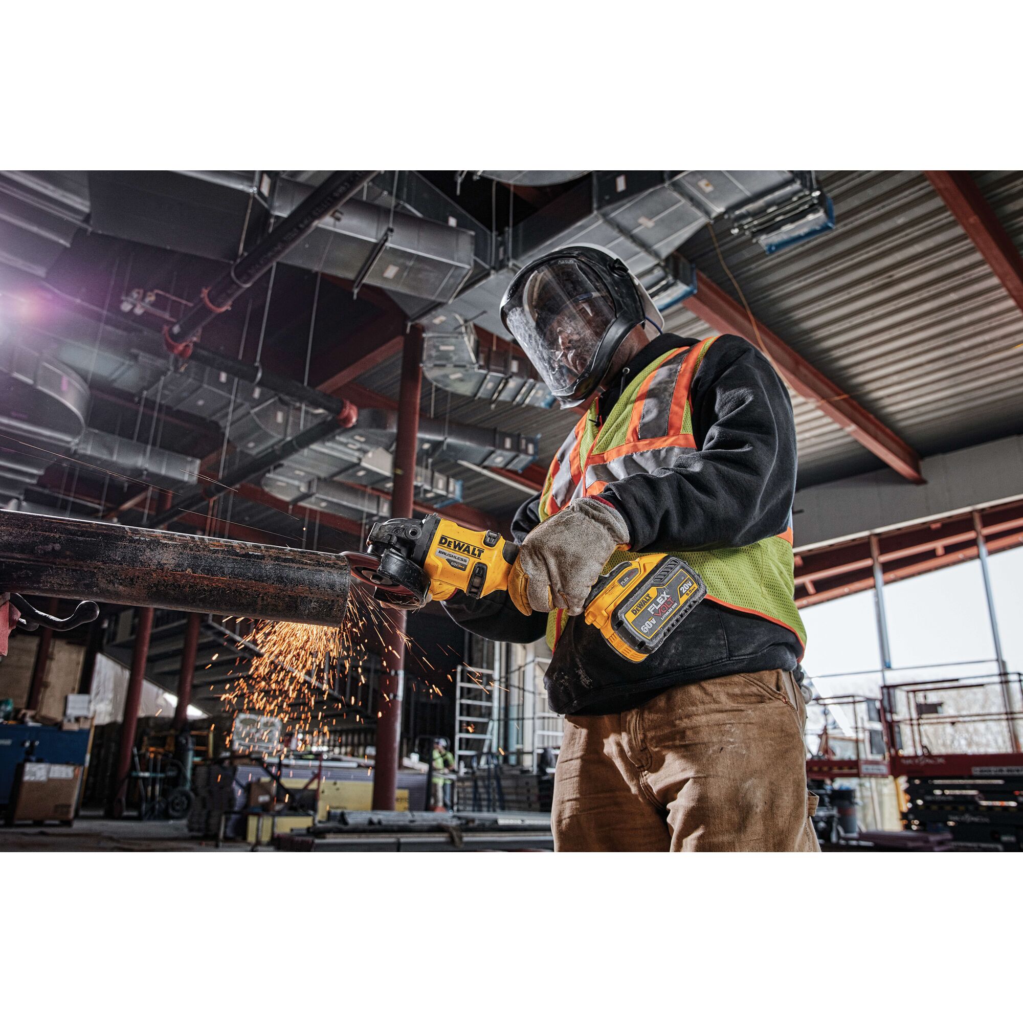 A person wearing protective gear and a safety vest operates a DEWALT power tool with a DCB609 battery, cutting a metal pipe and producing sparks inside an industrial construction site.