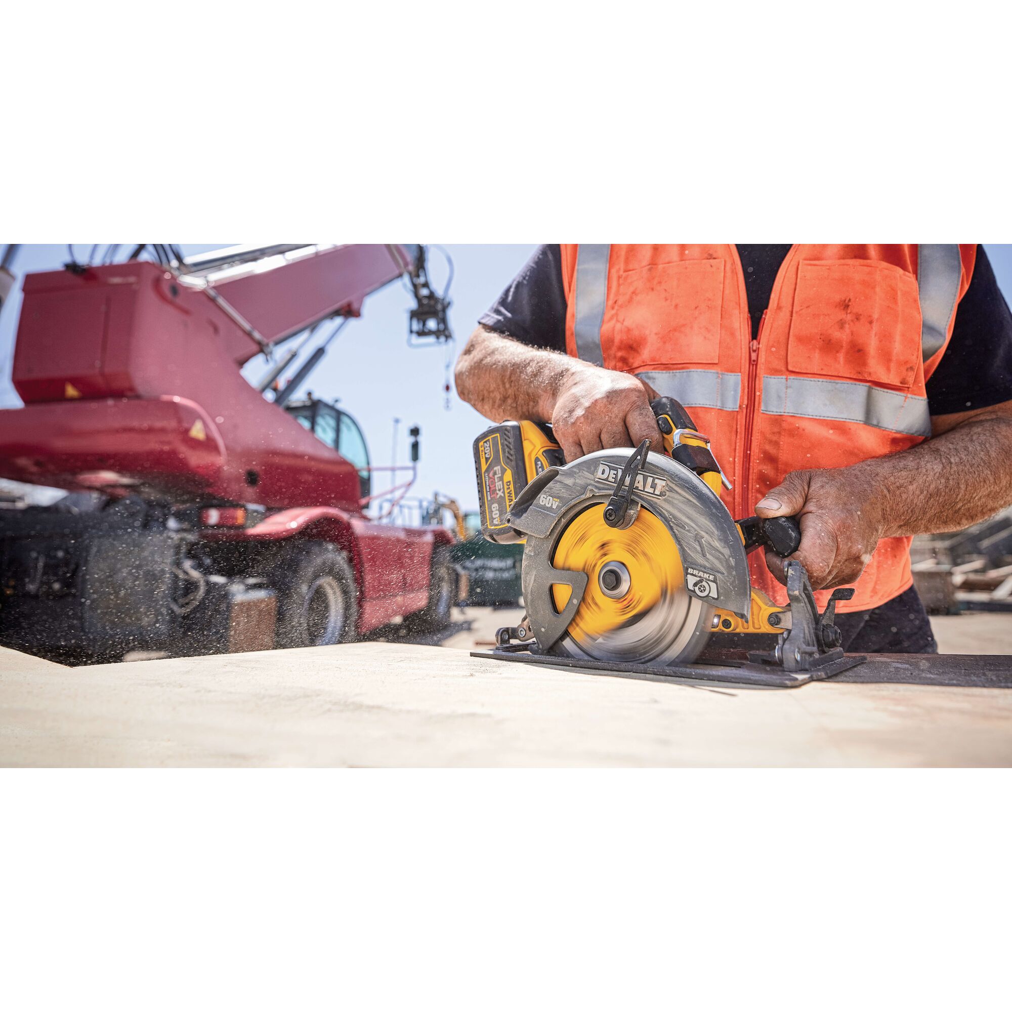 A person wearing an orange safety vest operates a DEWALT cordless circular saw on a wooden board at a construction site. A large red industrial vehicle is visible in the background.