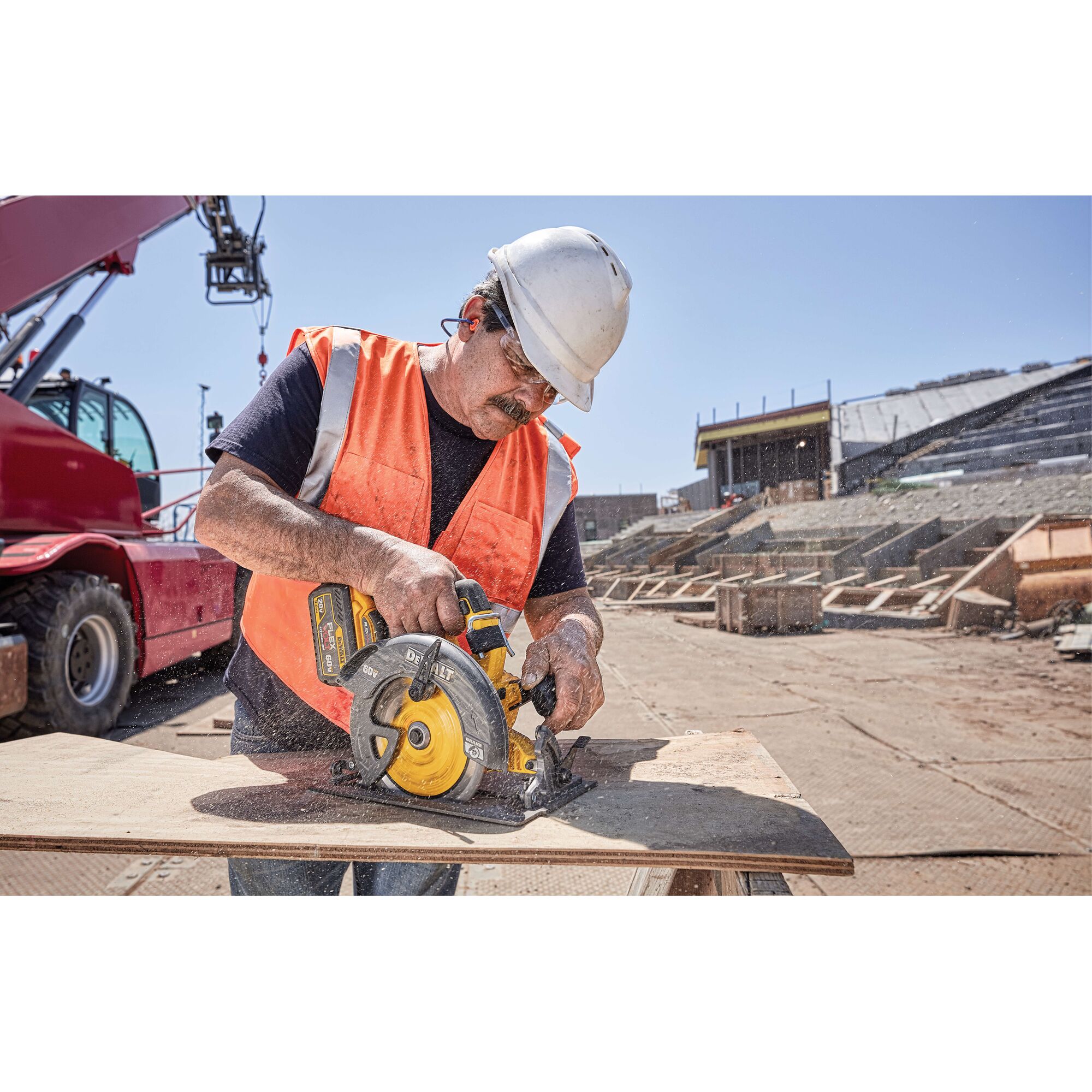 A construction worker wearing a white hard hat and orange safety vest uses a yellow and black DEWALT circular saw to cut a wooden board at an outdoor construction site. A red heavy machine and building structures are visible in the background.