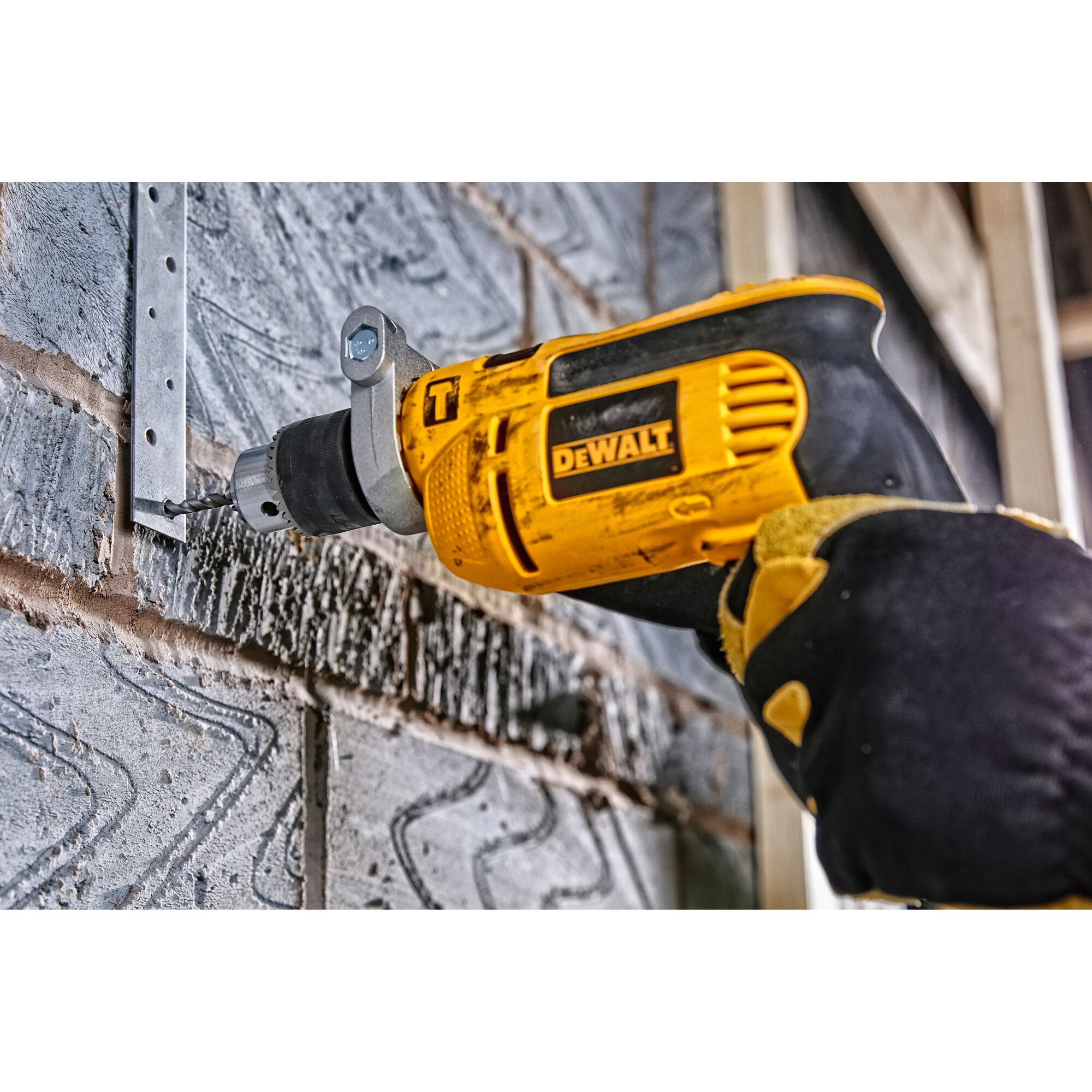 A person wearing work gloves is using a yellow and black DEWALT electric drill to drill into a brick wall near a metal bracket.
