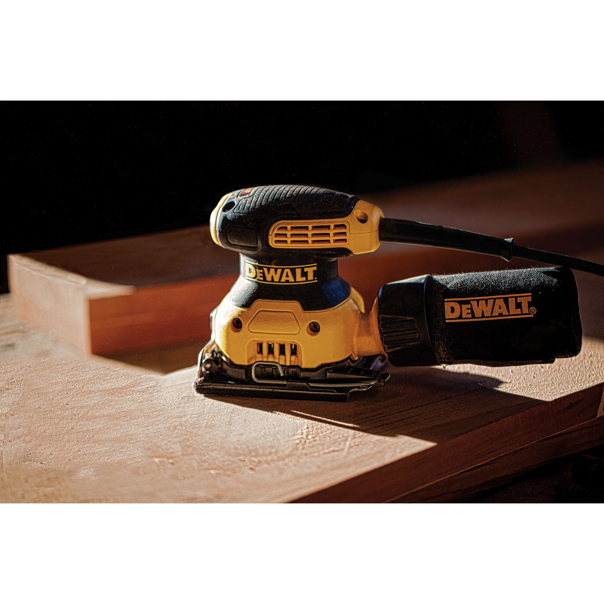 A DEWALT electric hand sander on a wooden surface, featuring a yellow and black design with a dust collection bag attached.
