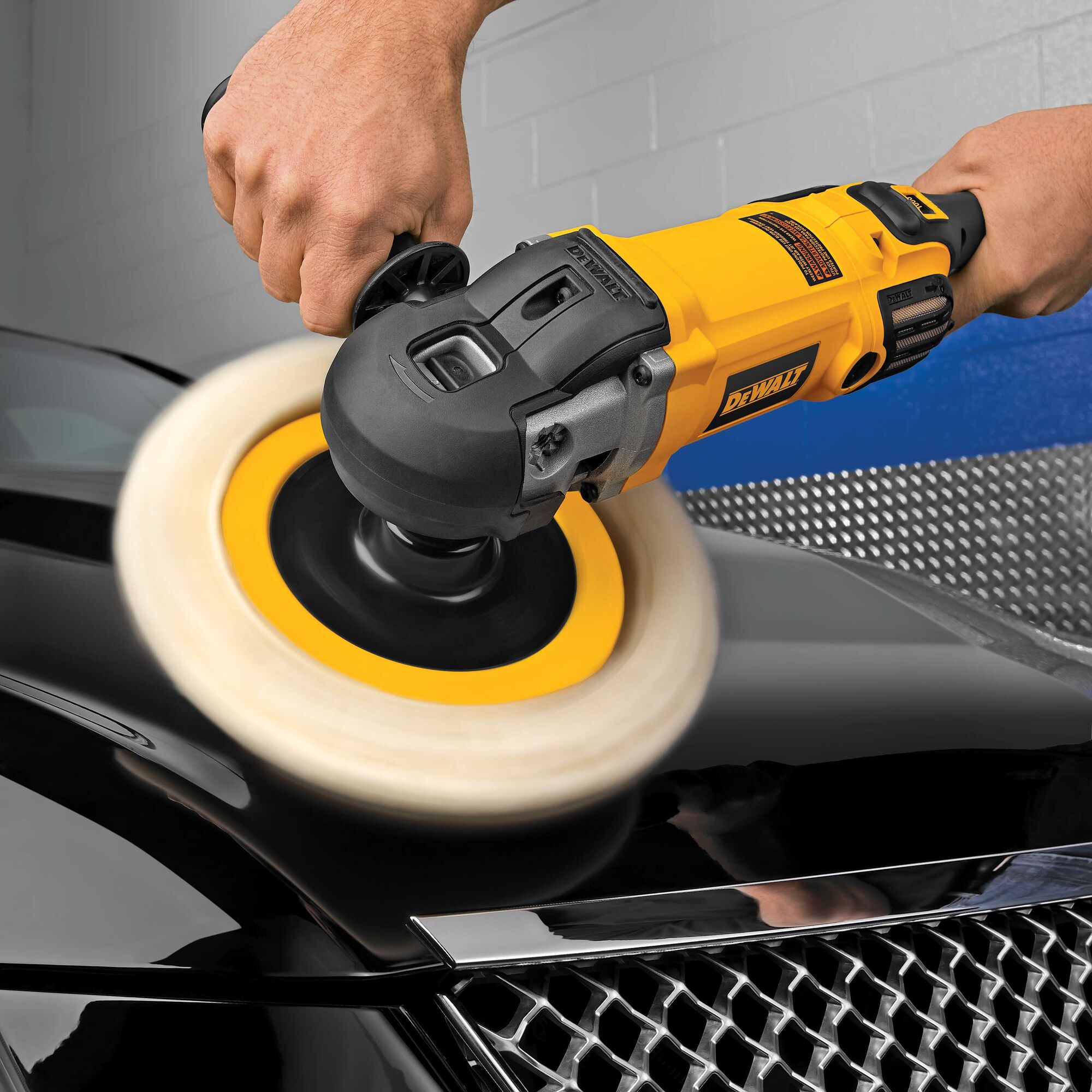 Close-up of a hand using a yellow and black electric polisher on the hood of a black car, polishing the vehicle’s surface.