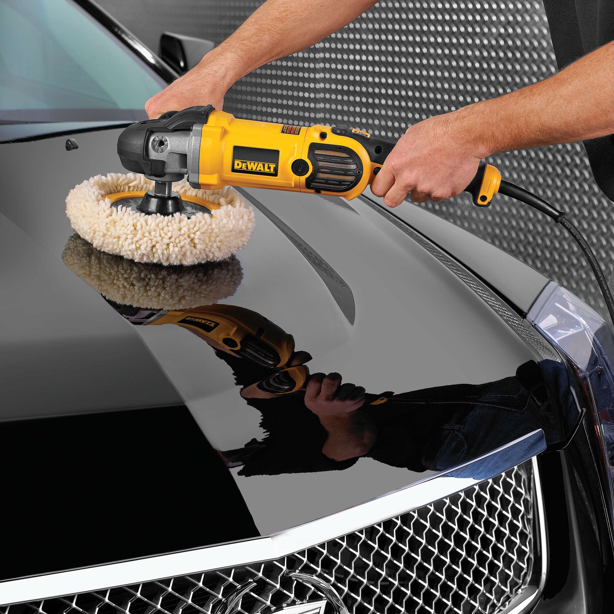 A person using a yellow DeWalt electric buffer to polish the hood of a black car.
